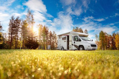 White RV parked in a sunny autumn meadow beside tall trees and a blue sky
