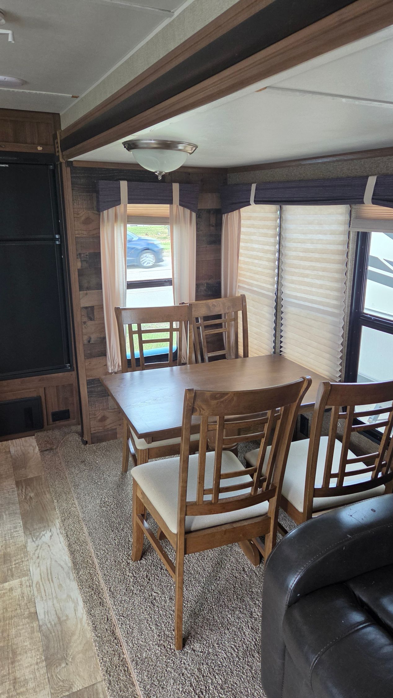 Wood-paneled RV dining area with wooden table and chairs, sofa, and bright windows with blinds