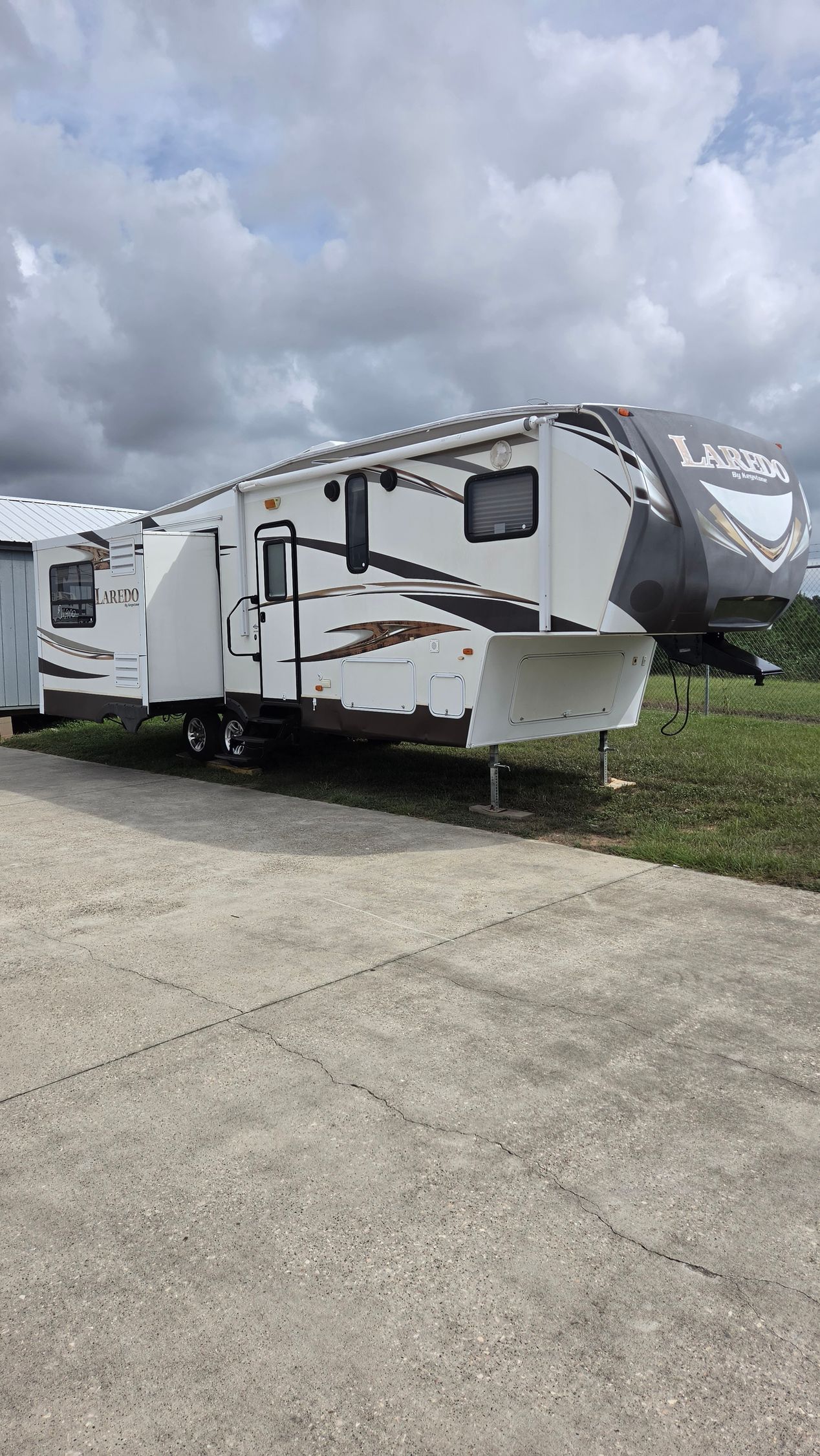 White travel trailer parked on a concrete lot under cloudy skies with another RV beside it