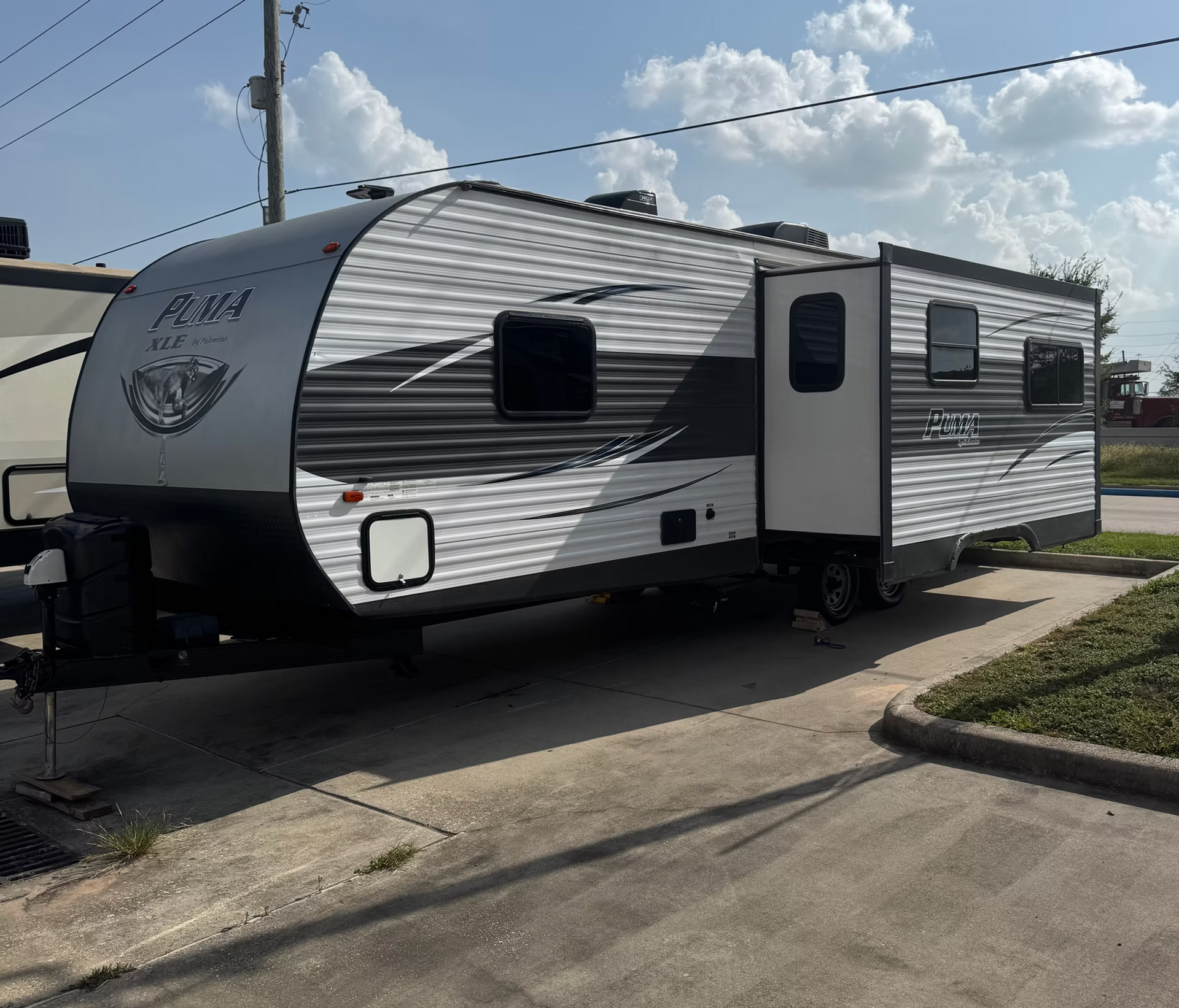 White and gray travel trailer parked beside a road under a bright sky