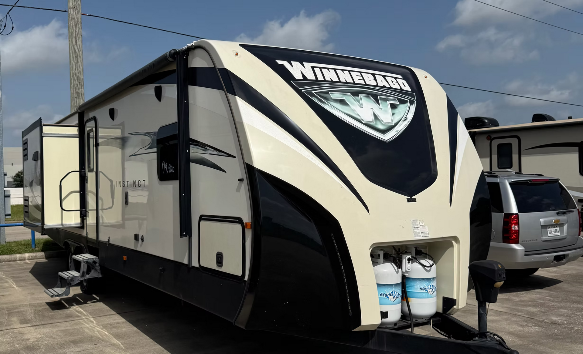 Black and white travel trailer parked outdoors with two propane tanks on the front.