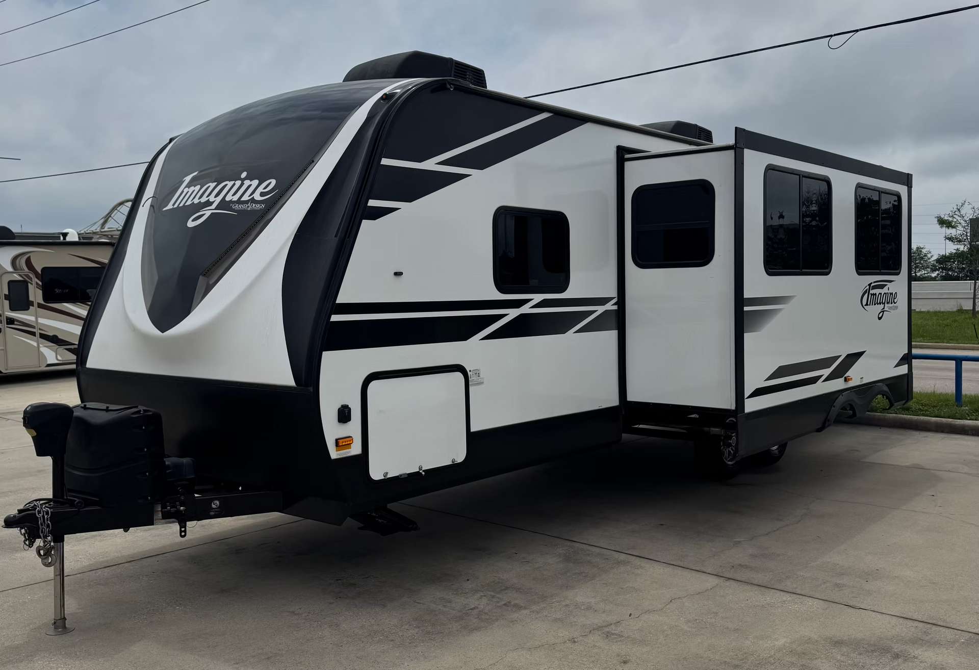 White and black travel trailer parked outdoors on pavement under an overcast sky