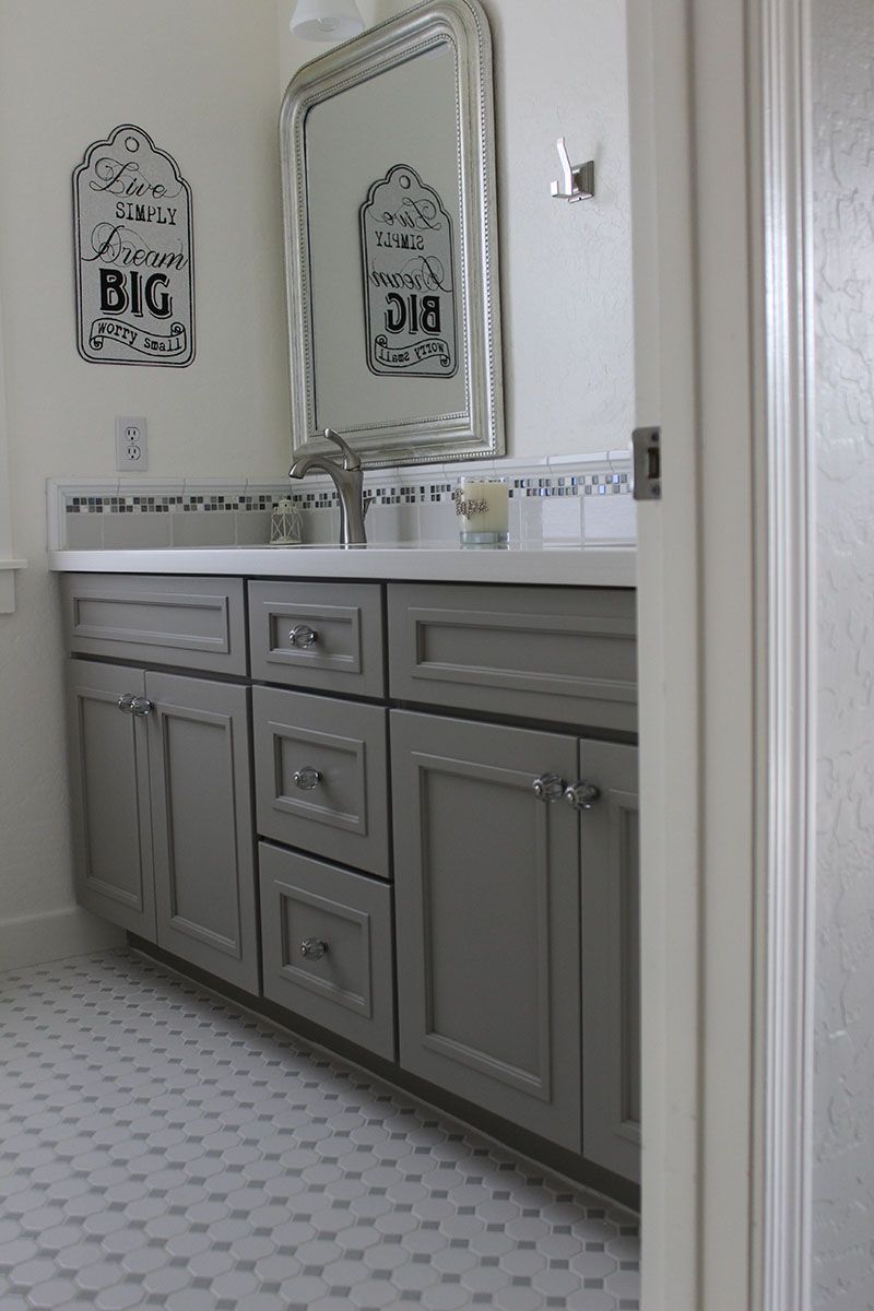 A bathroom with gray cabinets, a sink and a mirror.