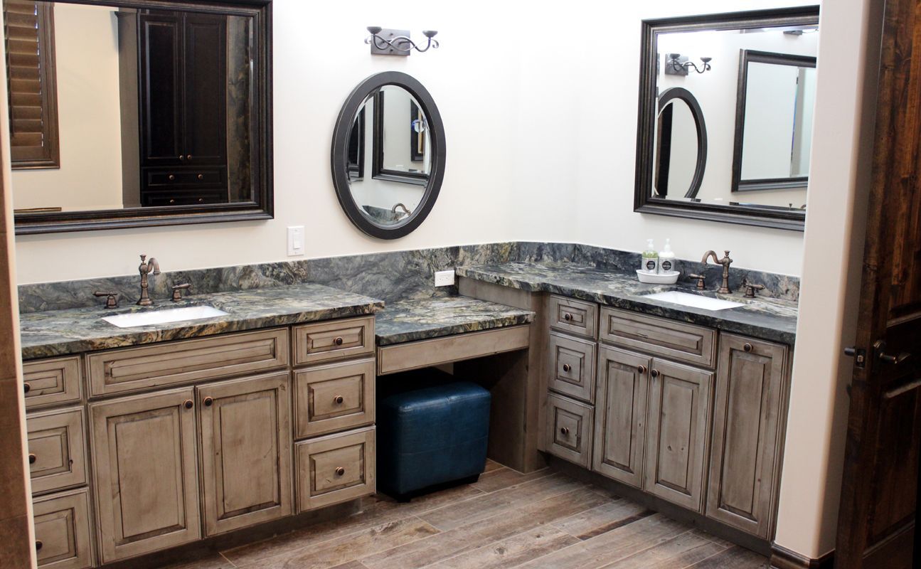 A bathroom with two sinks, two mirrors and a blue ottoman.