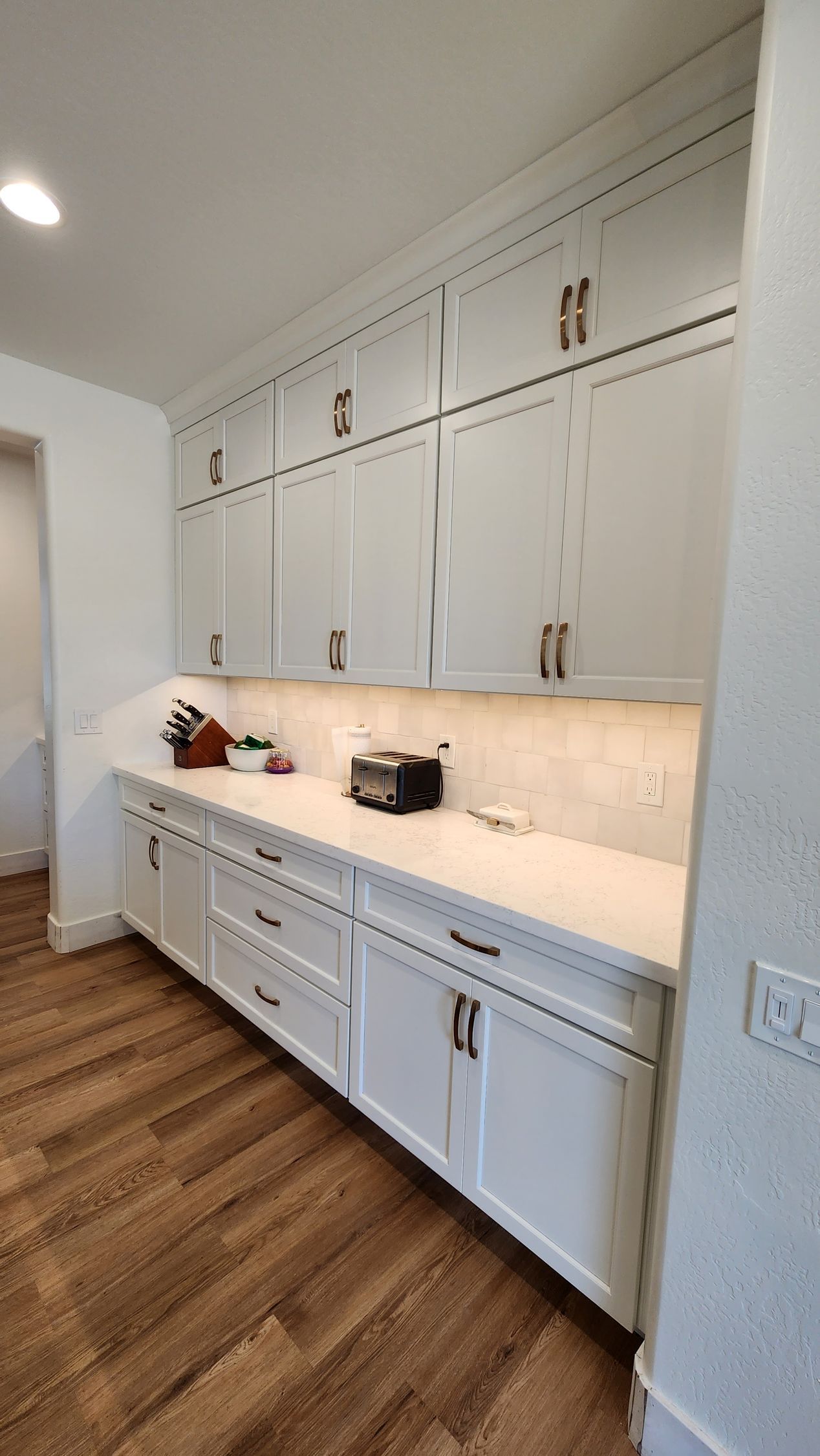 A kitchen with white cabinets and hardwood floors.