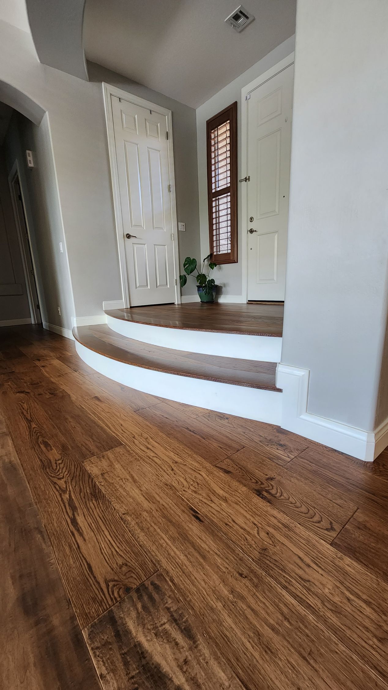 A hallway with hardwood floors and white stairs leading to a door.