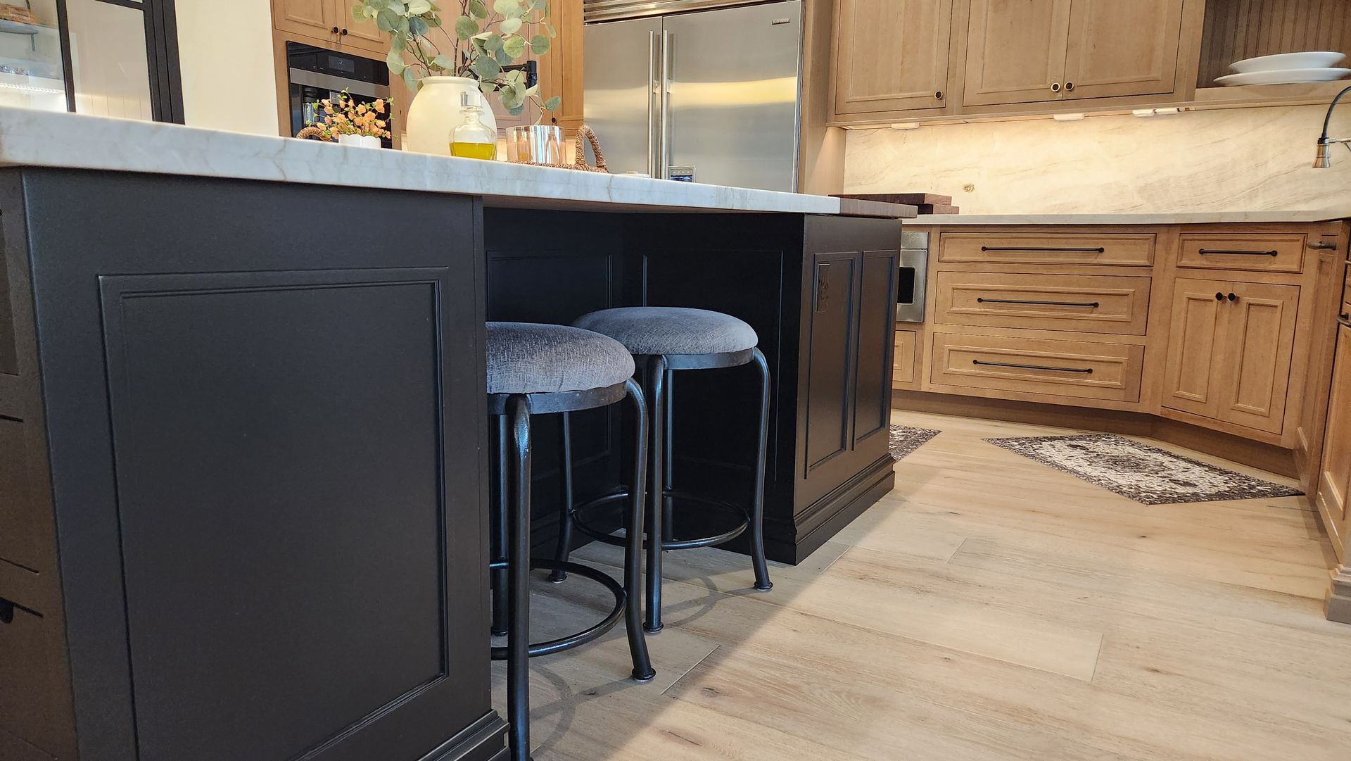 A kitchen with black cabinets and stools and a large island.