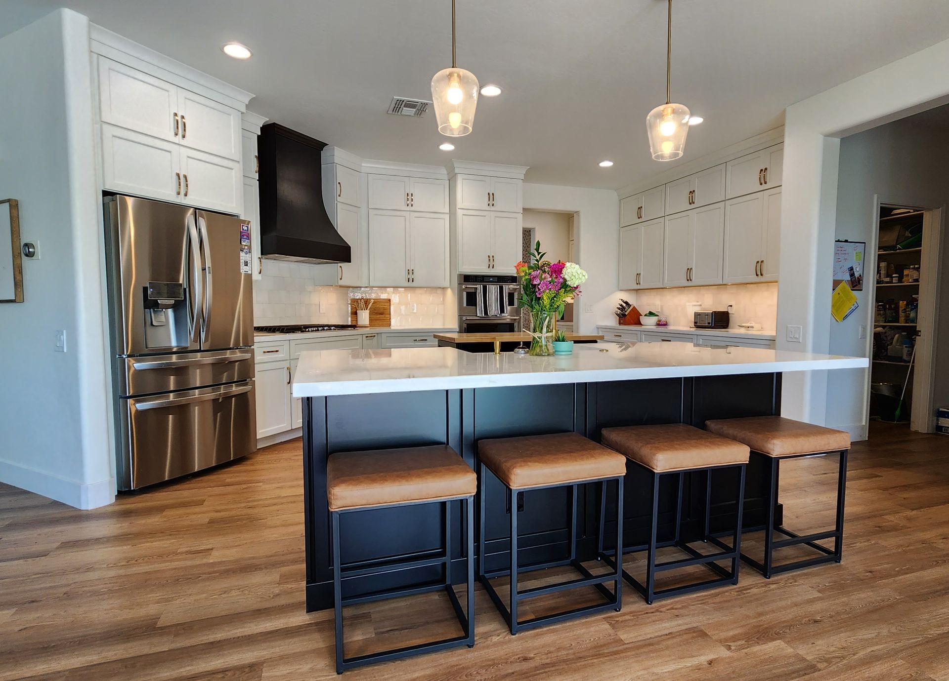 A kitchen with a large island, stools, and a refrigerator.