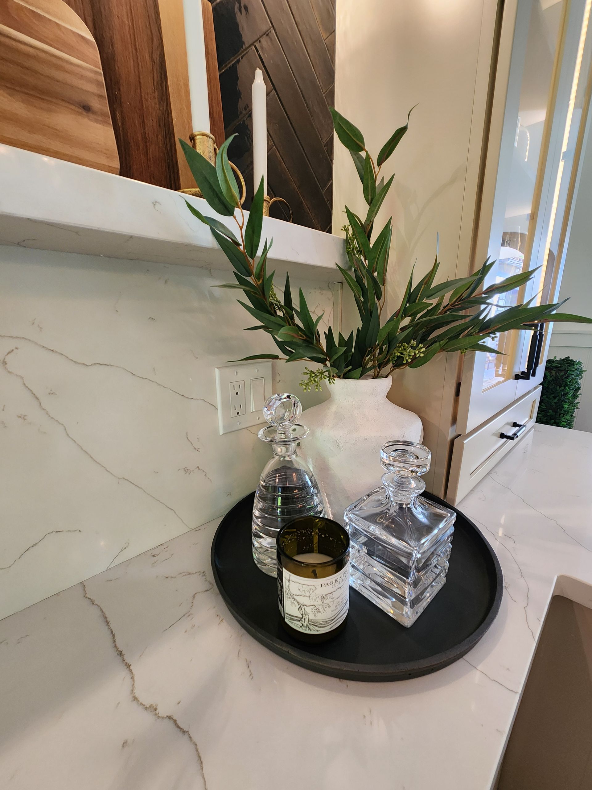 A tray with a vase of flowers and two decanters on it is on a counter.