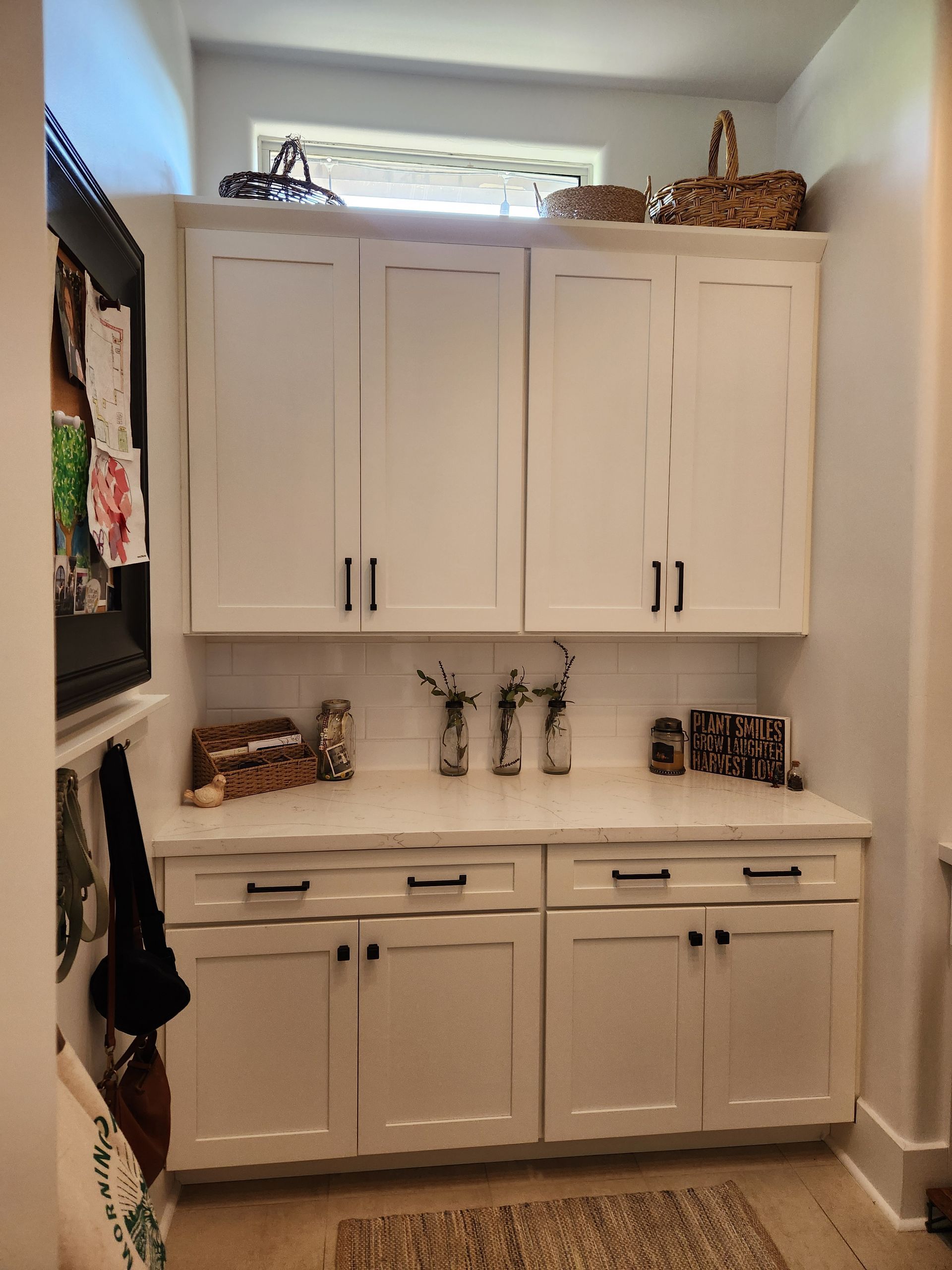 A laundry room with white cabinets and a window