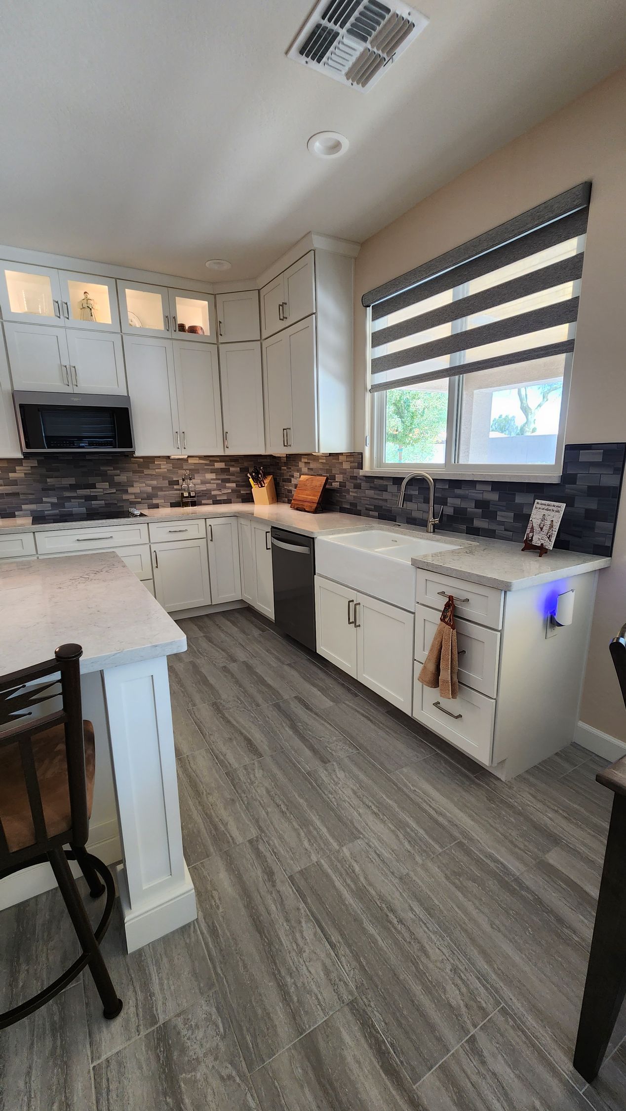 A kitchen with hardwood floors, white cabinets, stainless steel appliances, and a large window.