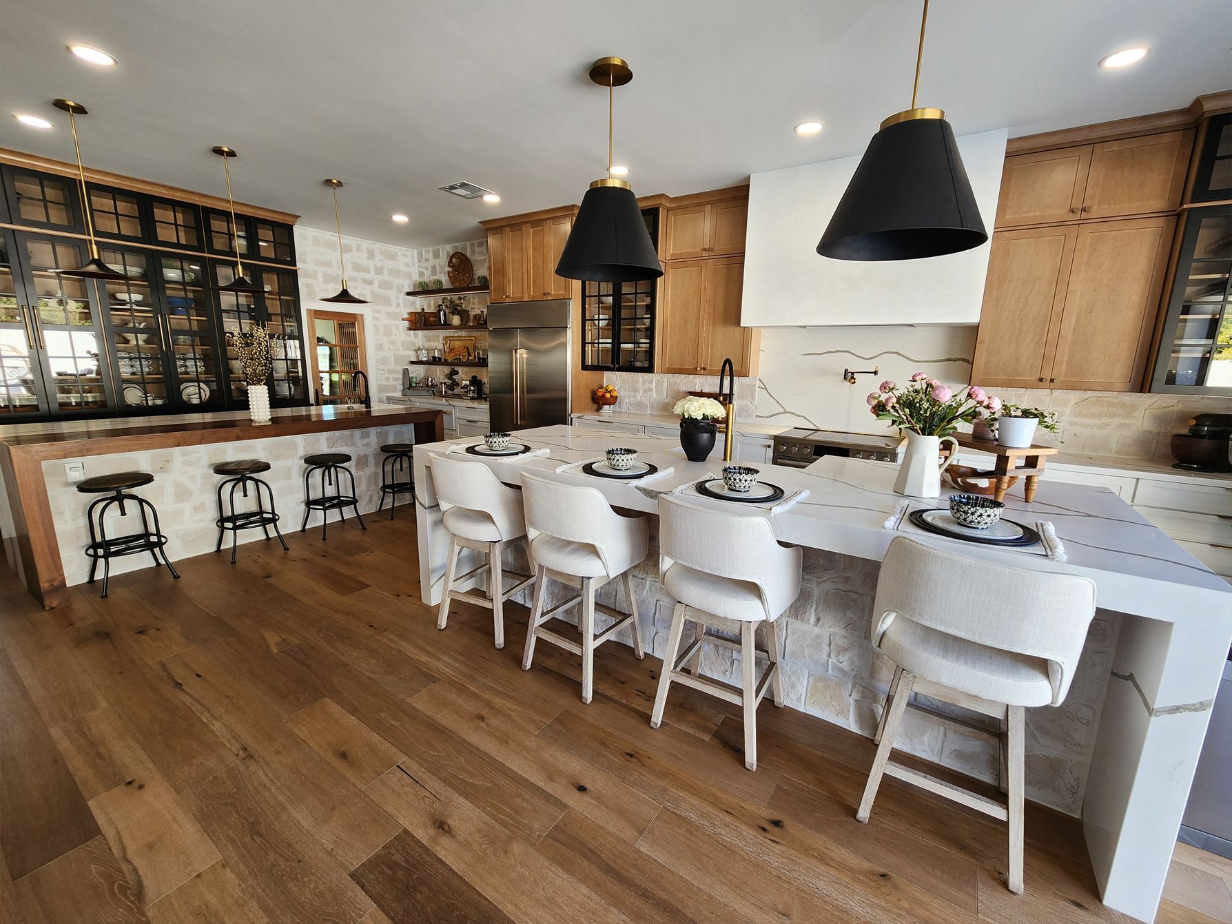 A kitchen with a large island, stools, and a dining table.
