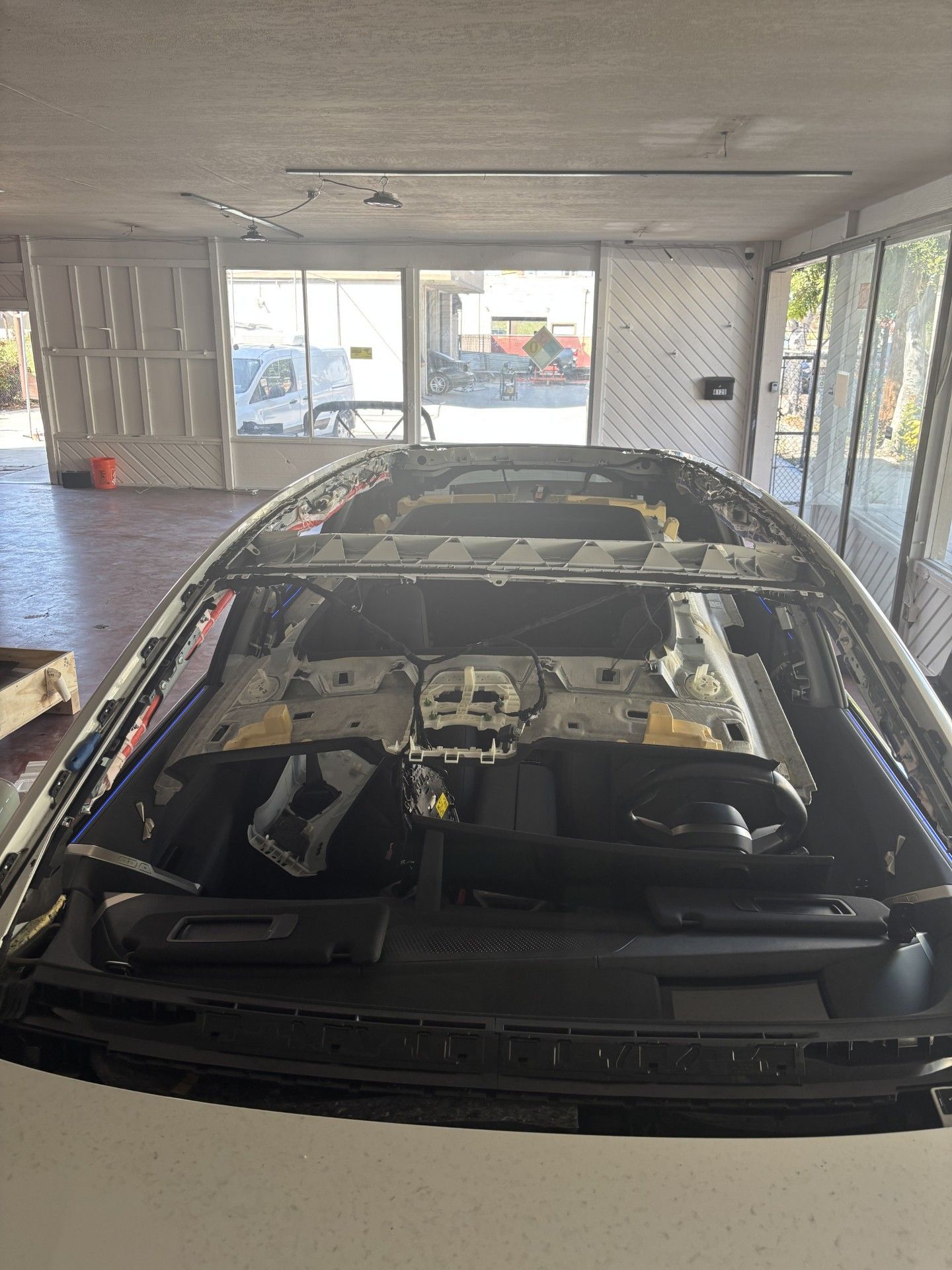 Car partially disassembled in a garage, with a visible stripped roof and windshield in front.