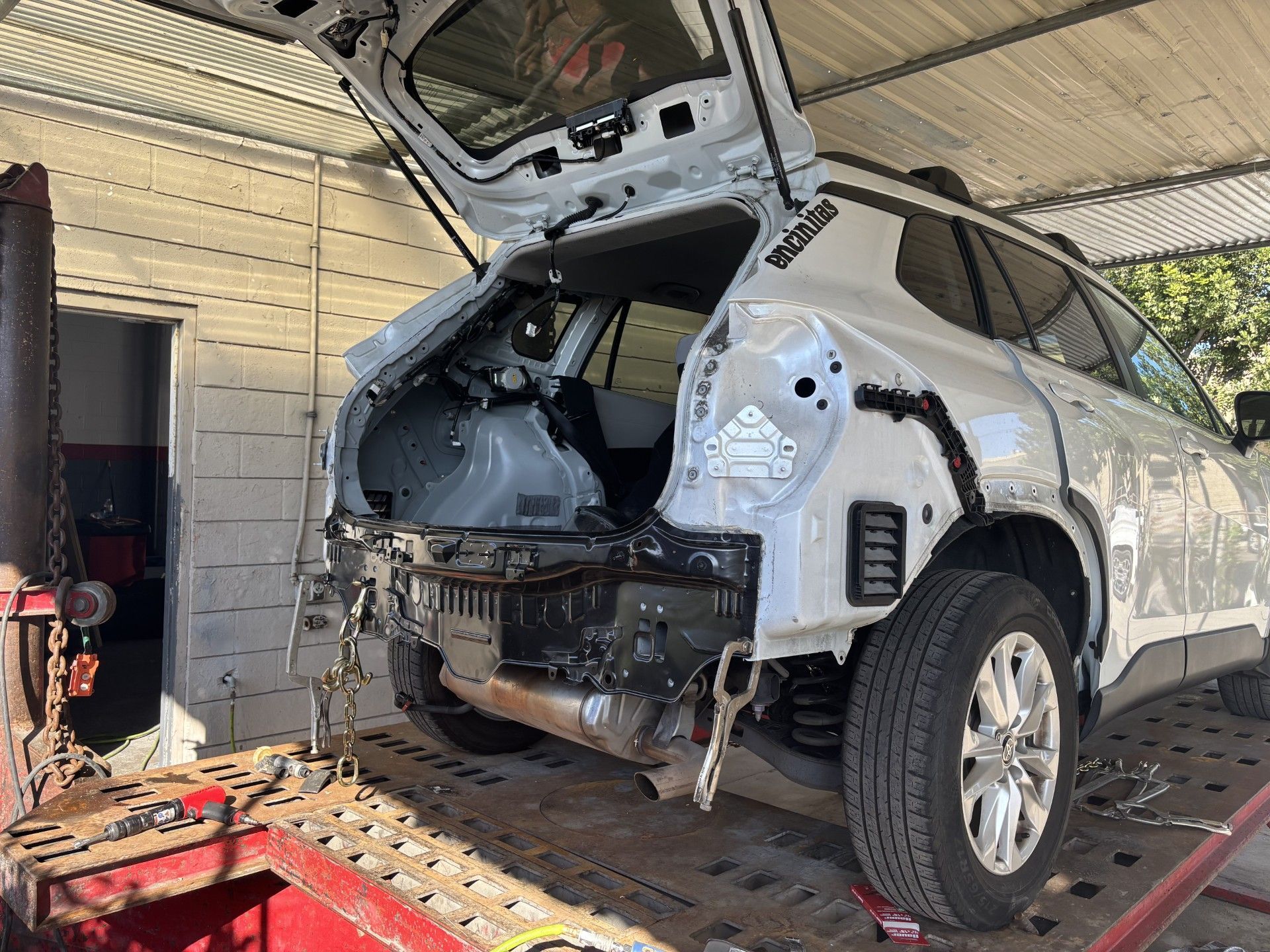 SUV with rear body panels removed in an auto repair shop, exposing the trunk area and frame