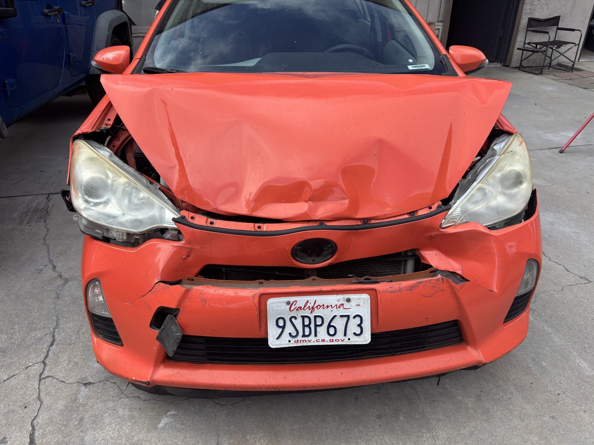 Front view of a heavily damaged red car with a crushed hood and broken headlights.