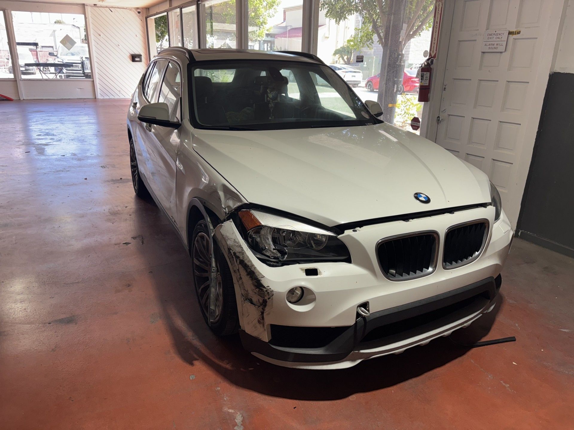 White BMW SUV parked in a covered driveway with front-end damage on the left side
