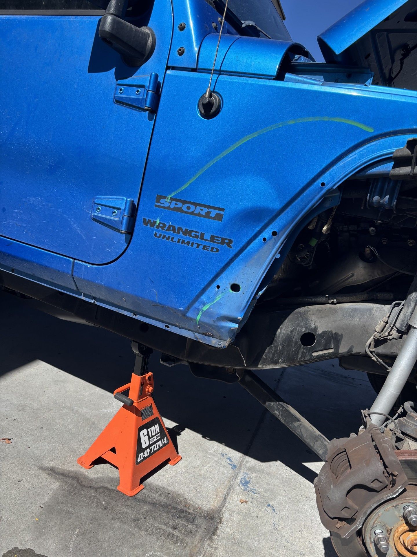 Blue Jeep on jack stands with wheel removed, showing exposed suspension and brake assembly.