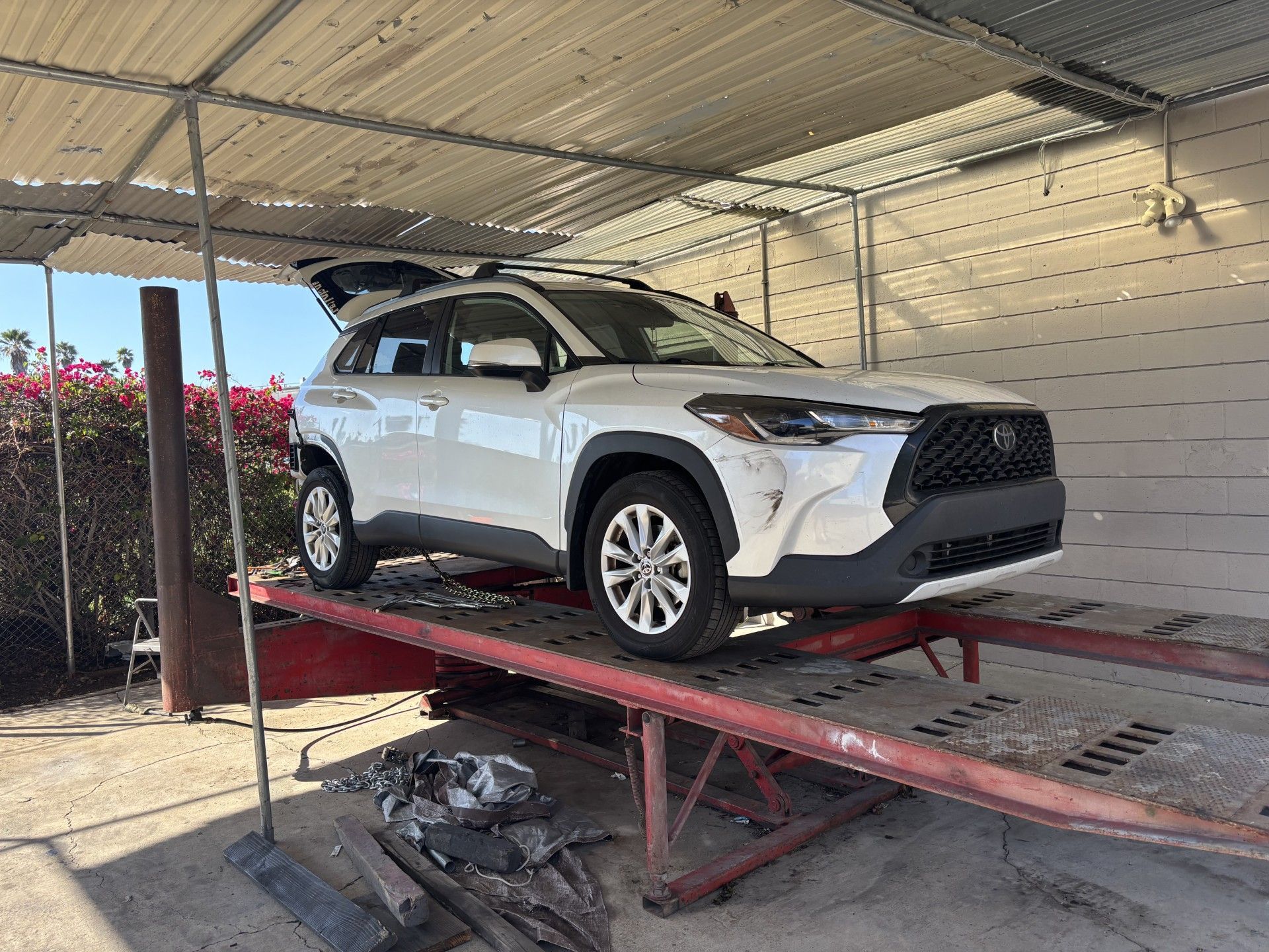 White SUV on a red hydraulic lift under a covered carport, with its hatch open.