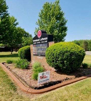A brick sign for Immanuel Lutheran Church, School, and Childcare surrounded by green shrubs and a small lawn.