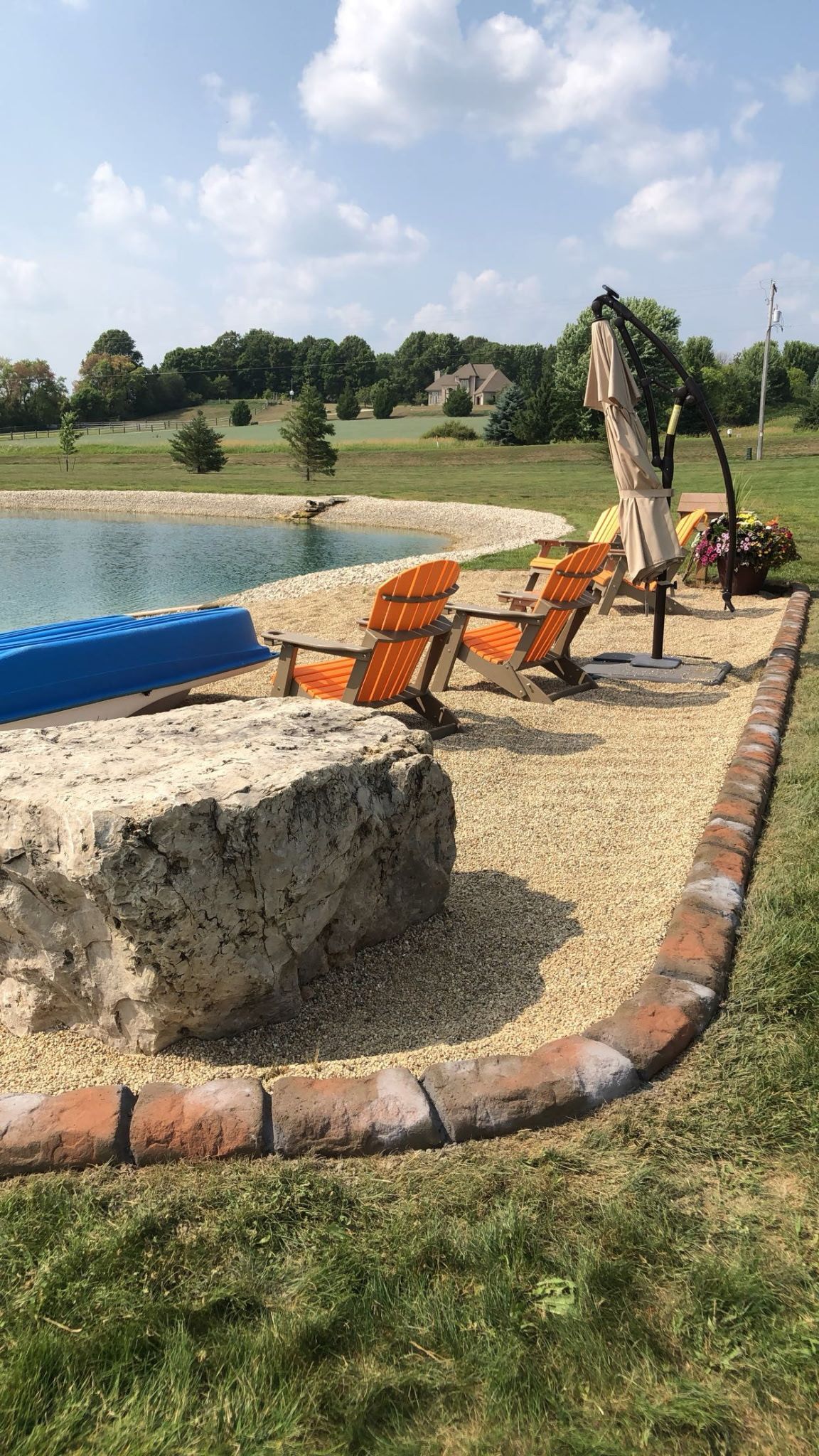 Small backyard pool area with orange lounge chairs, a thatched umbrella, and a brick-edged gravel path.