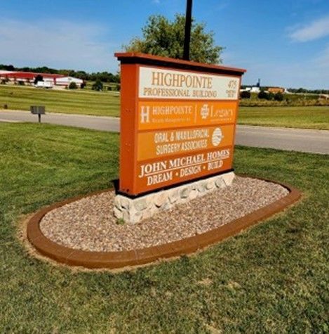 A multitenant directory sign for Highpointe Professional Building sits in a landscaped rock bed surrounded by grass.