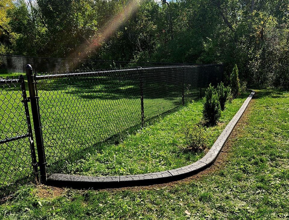 A curved stone garden border separates a patch of grass and small shrubs from a fenced-in lawn area.