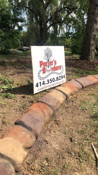 A business sign for Porter's Borders stands next to a newly installed decorative stone landscape edging in a yard.