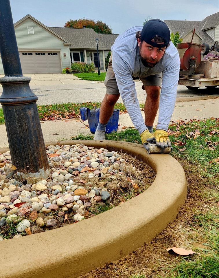 A person kneeling on a lawn, smoothing a newly poured concrete landscape border around a lamp post.