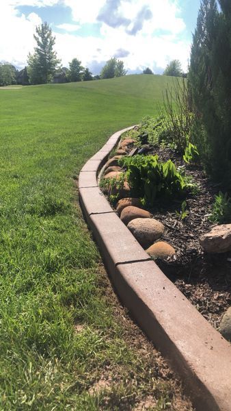 A curved stone garden border separates a manicured green lawn from a landscaped garden bed with mulch and shrubs.