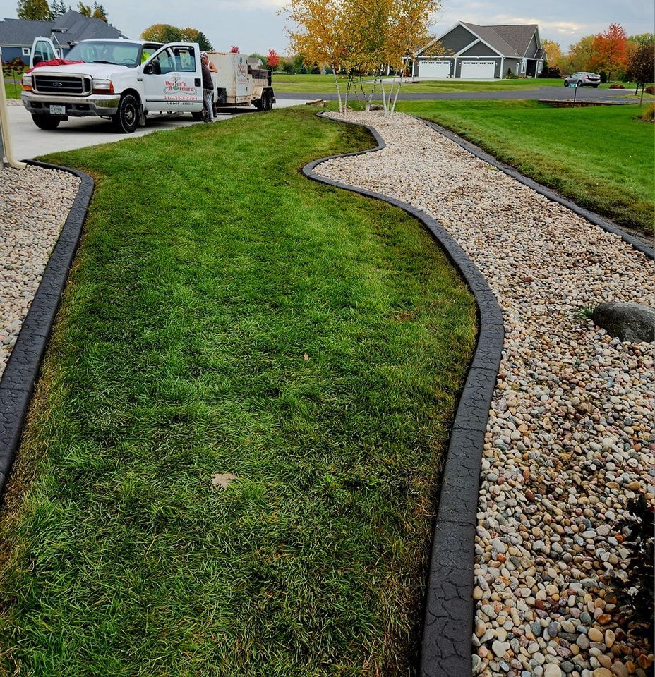 A lawn with a curving, black-edged border separating green grass from a gravel pathway, with a service truck in the back.