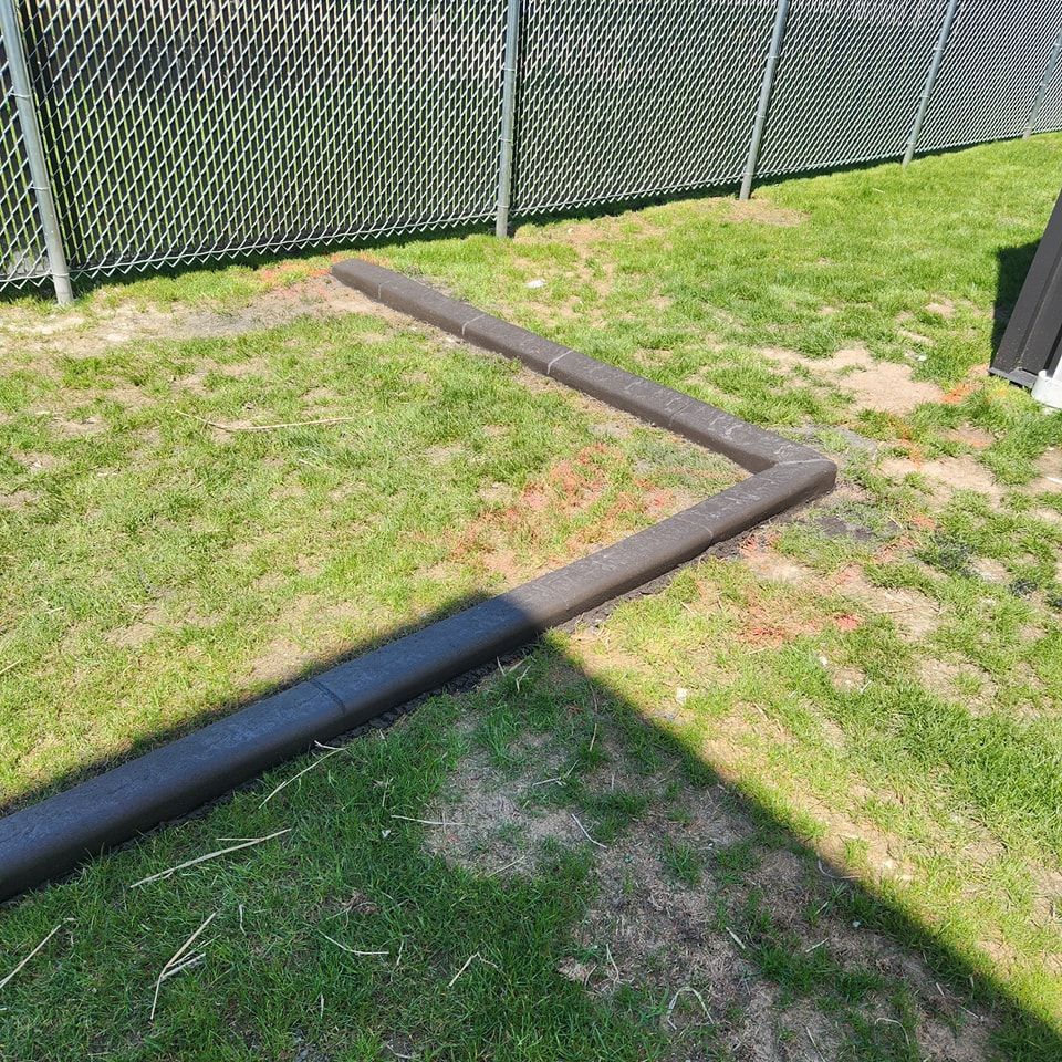 Two dark-colored plastic garden edgers laid on a grassy lawn in an L-shape near a chain-link fence.