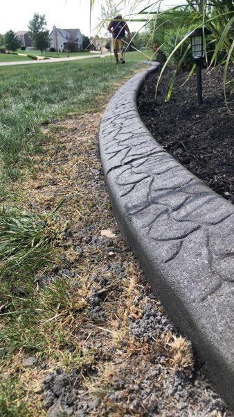 A person walks on a lawn behind a curved, gray concrete garden border with a textured, stamped pattern.