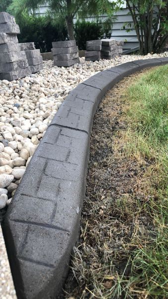 A close-up of a stamped concrete garden border separating light-colored decorative landscape rocks from a grassy lawn.