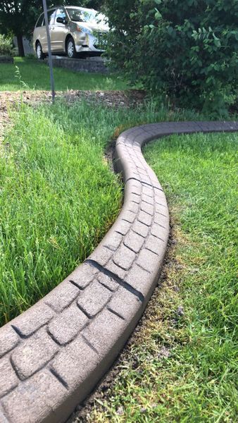 A curved, brown, faux-stone concrete landscape edging separates a lawn from a garden bed.