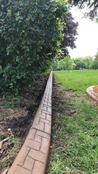 A long, tan concrete landscape border with a brick-patterned stamp separates a garden bed from a grassy lawn.