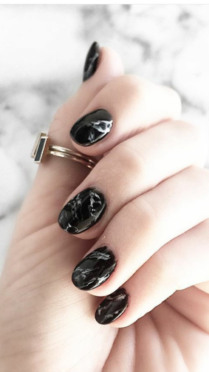 A woman 's hand with black nails and a ring