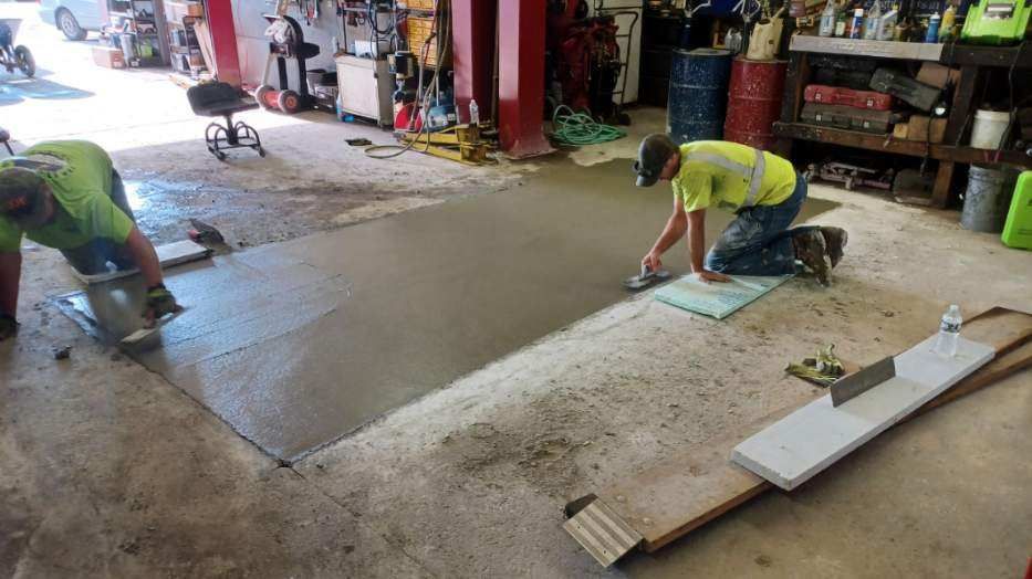 Two men are working on a concrete floor in a garage.