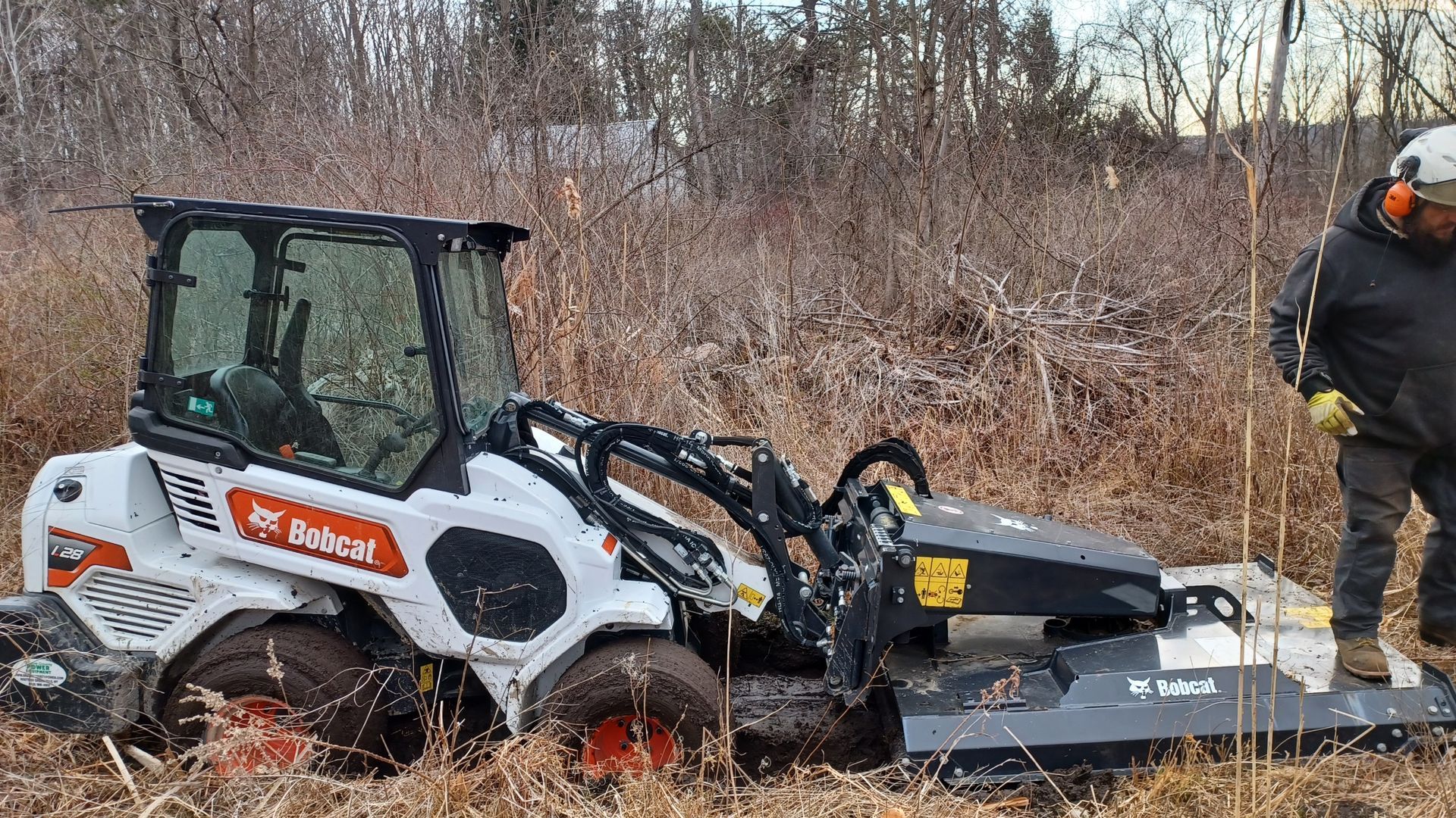 A man is standing next to a bobcat tractor in a field.