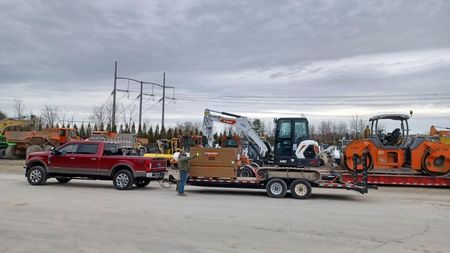 A red truck is towing a trailer with an excavator on it.