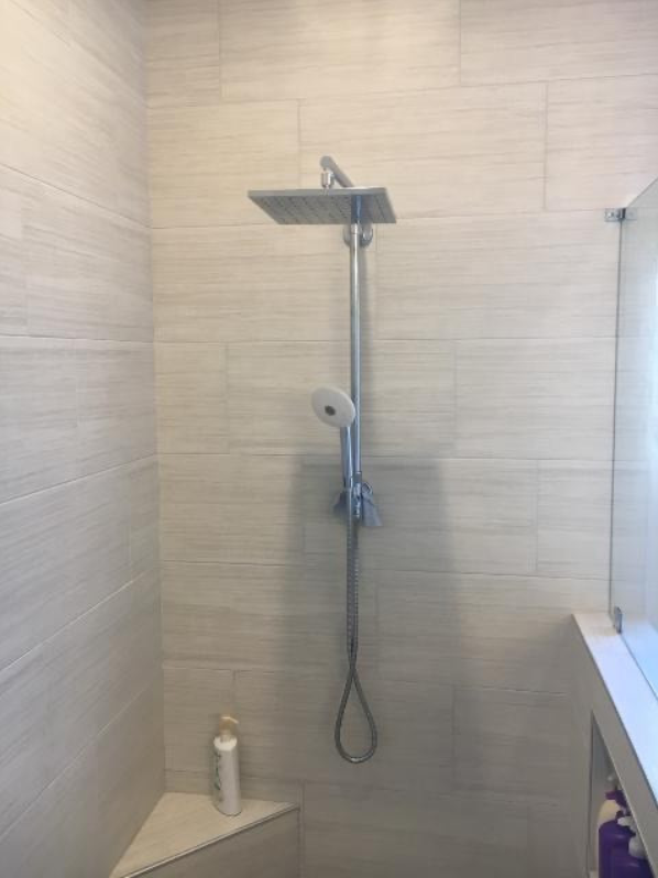 A bathroom with a shower head and a corner seat.