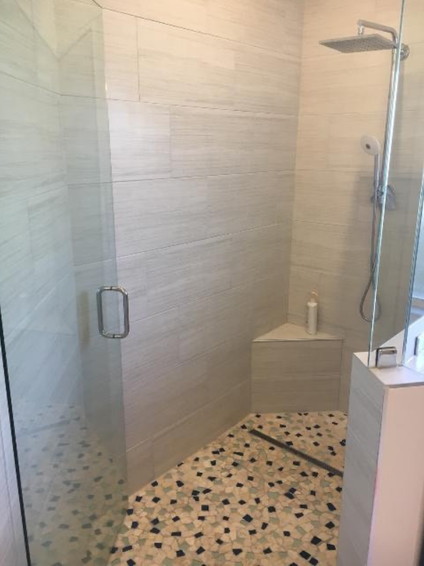A bathroom with a walk in shower with a tiled floor and a shower head.