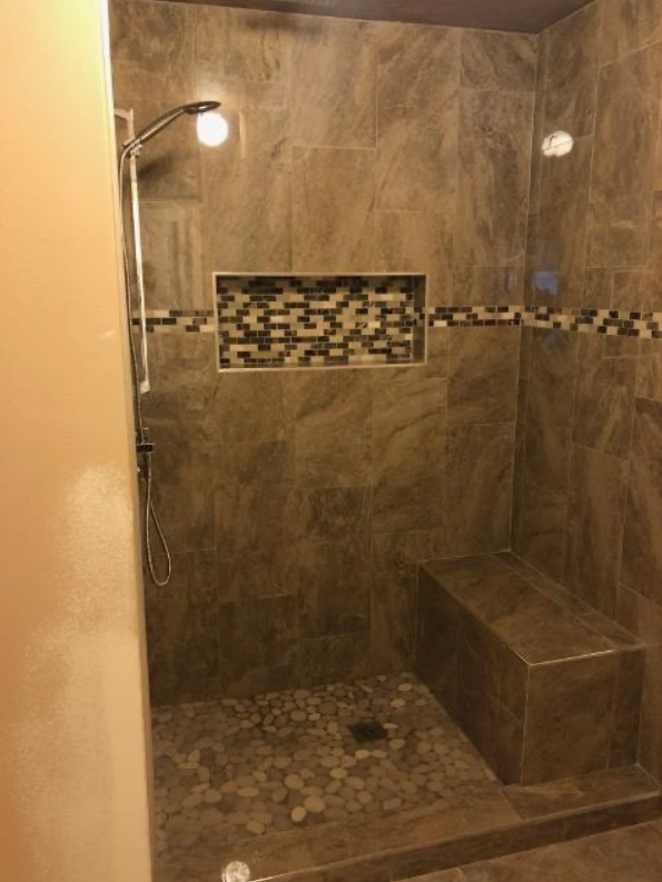 A walk in shower with a bench and a shower head.