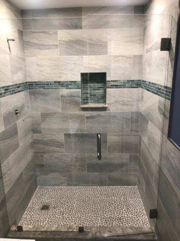 A walk in shower with a glass door and tiled walls.