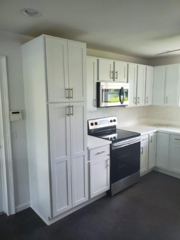 A kitchen with white cabinets , a stove , and a microwave.