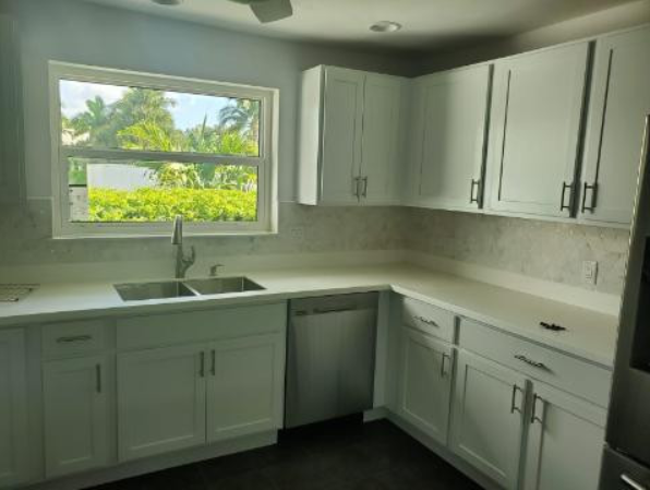 A kitchen with white cabinets , a sink and a window