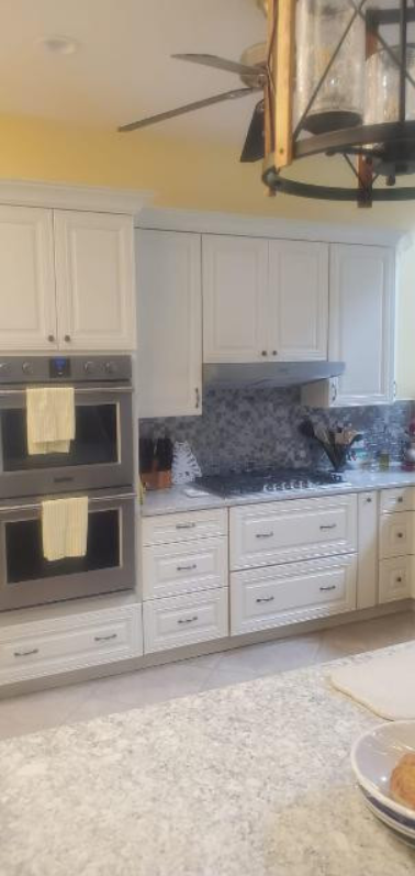 A kitchen with white cabinets , stainless steel appliances and a ceiling fan.
