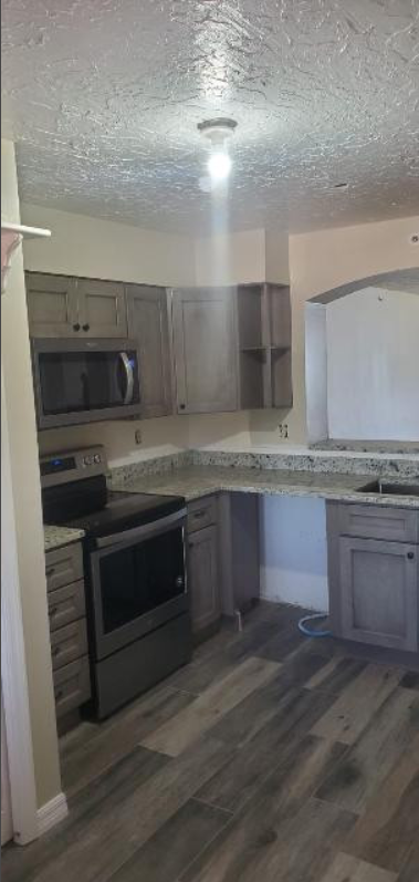 A kitchen with a stove , microwave , sink and cabinets.