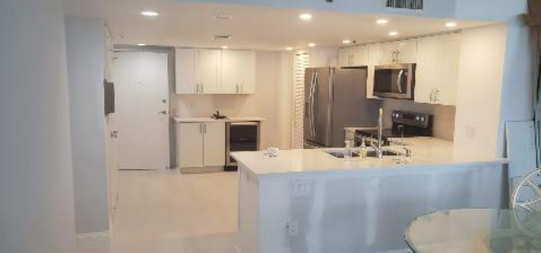A kitchen with white cabinets , stainless steel appliances , a refrigerator and a sink.