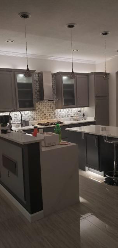 A kitchen with gray cabinets , white counter tops , and a large island.