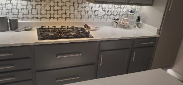 A kitchen with gray cabinets and a stove top oven.